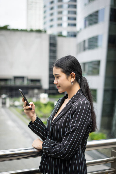 Jovem mulher de negócios asiática usando no celular smartphone.Young profissional feminino na cidade em frente ao grande edifício
. - Foto, Imagem