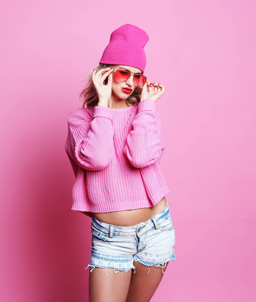 Fajna, wesoła dziewczyna z jasne czerwone usta nosi nowoczesne czapka i różowy sweter. Hipster stylu. Mody młodzieżowej. Różowy tło. - Zdjęcie, obraz
