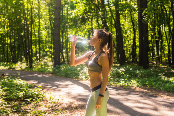 Fitness hermosa mujer bebiendo agua y sudoración después de hacer ejercicio en verano día caluroso en el parque. Atleta femenina después del entrenamiento
. - Foto, Imagen