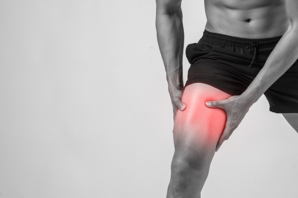 Νέος αθλητισμός άνθρωπος με ισχυρή γυμνασμένα πόδια κρατώντας τα γόνατα με τα χέρια του στον πόνο μετά από να υποστεί ζημία συνδέσμων απομονωθεί σε λευκό. - Φωτογραφία, εικόνα
