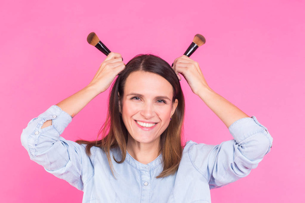 Funny makeup artist with brushes on pink background - 写真・画像