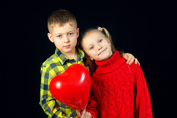 Des enfants sur un fond sombre. Garçon et fille avec ballon rouge. Le concept de l'amitié des enfants
 - Photo, image