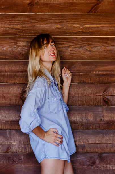 beautiful blonde girl in men's shirt on the background of wooden wall - Фото, изображение