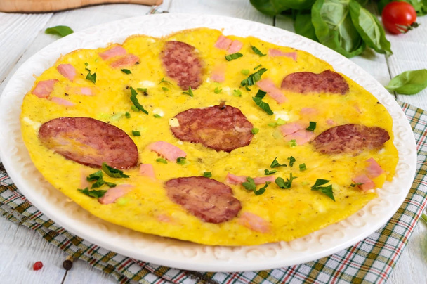 Omelette con prosciutto, salame, formaggio e verdure su un piatto su uno sfondo di legno bianco. Colazione
. - Foto, immagini