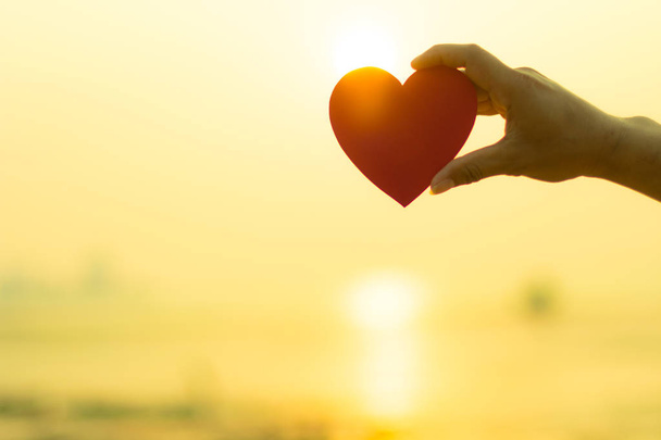 Χέρι που κρατά το σχήμα καρδιάς αγάπη κόκκινο χαρτί σε φόντο παραλία. Lov - Φωτογραφία, εικόνα