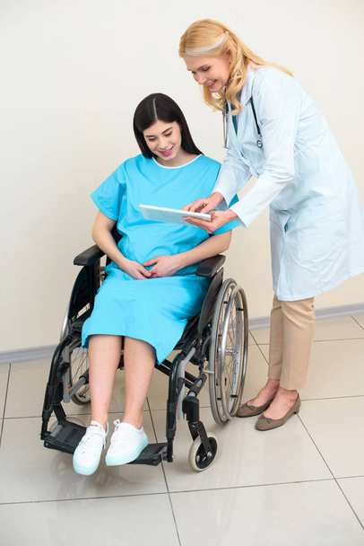 obstetrician gynecologist showing digital tablet to pregnant woman on wheelchair - Foto, Imagem