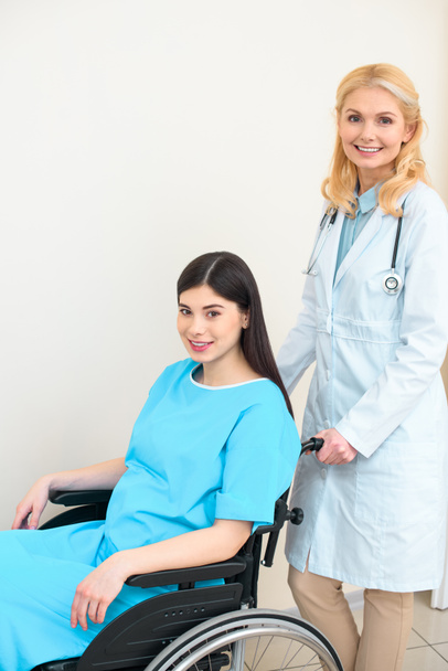 счастливый акушер-гинеколог верхом на беременной женщине на инвалидной коляске в родильном доме и смотрит в камеру
 - Фото, изображение