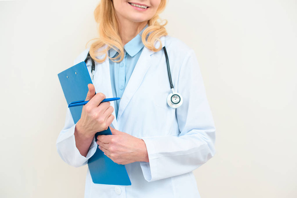 cropped shot of smiling female doctor with clipboard on white - Valokuva, kuva