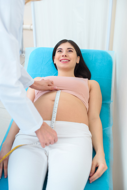 mérés a terhes nő hasa mérete mérőszalaggal a kanapé szülész-nőgyógyász - Fotó, kép