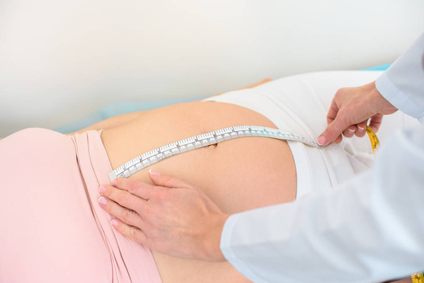tiro recortado de ginecólogo obstétrico que mide el tamaño del vientre de la mujer embarazada con cinta métrica
 - Foto, Imagen