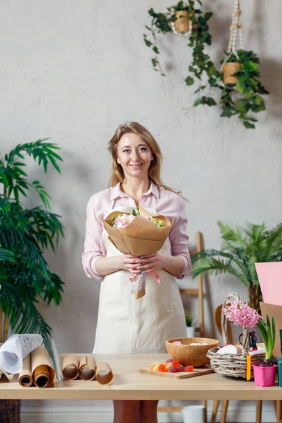 Photo of smiling florist in apron with bouquet of flowers with kraft paper - Фото, зображення