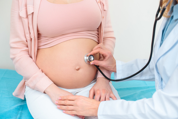 cropped shot of obstetrician gynecologist listening heartbeat of child fetus of pregnant woman with stethoscope - Fotografie, Obrázek