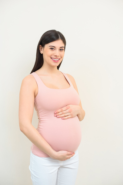 feliz joven embarazada sosteniendo su vientre en blanco
 - Foto, Imagen