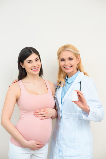 акушер гінеколог і вагітна жінка з баночкою таблеток, дивлячись на камеру
 - Фото, зображення