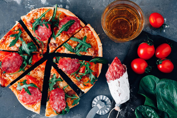 Pizza with ingredients on a black background, salami, spinach, tomatoes and beer. - 写真・画像