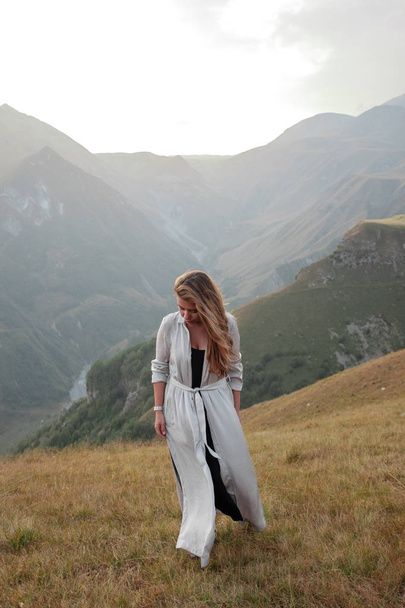Beautiful young woman in a long dress is standing in the valley of the mountains - Foto, afbeelding