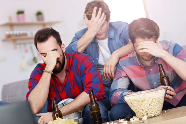 Sad male group of friends watching sports on tv at home - Photo, Image