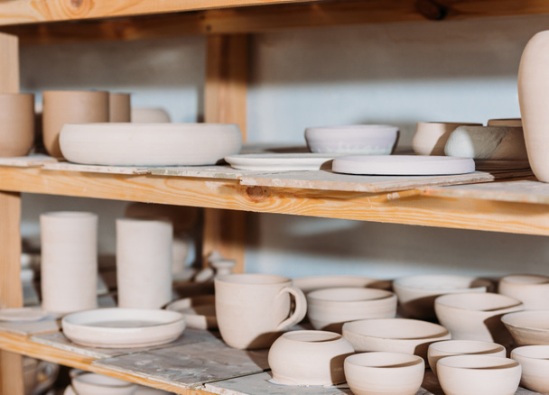 close up of ceramic plates and bowls on wooden shelves in pottery workshop - Foto, Imagen
