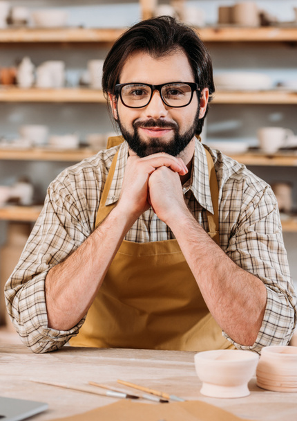 portrait of smiling potter in apron sitting in workshop - Photo, Image