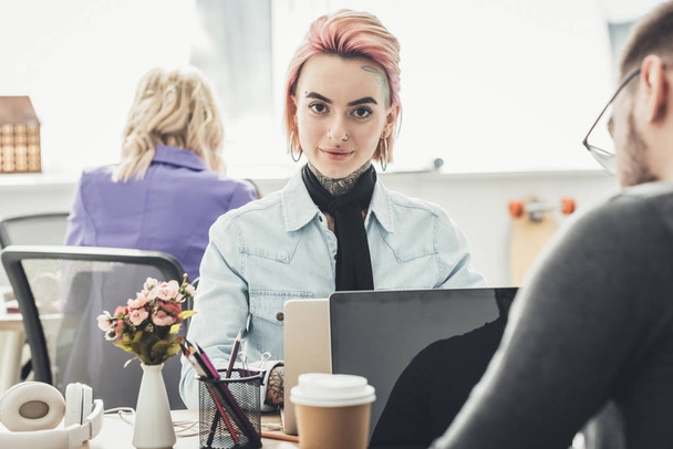 selective focus of tattooed businesswoman at workplace with colleagues near by in office - Photo, Image
