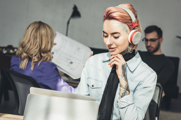 enfoque selectivo de mujer de negocios tatuada en auriculares en el lugar de trabajo en la oficina
 - Foto, imagen