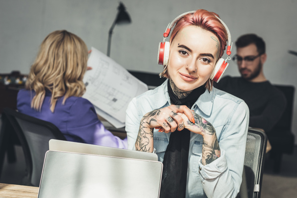Selektiver Fokus tätowierter Geschäftsfrau mit Kopfhörer am Arbeitsplatz im Büro - Foto, Bild