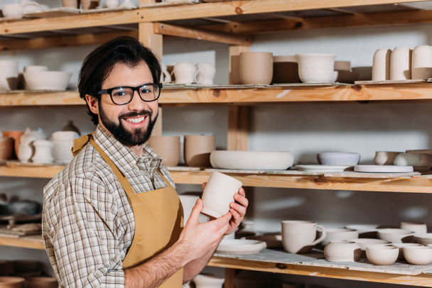 mosolyogva potter gazdaság kerámia csésze, étkészlet a polcokon a műhelyben - Fotó, kép