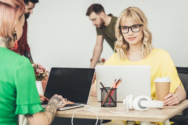 focus selettivo di giovani blogger in occhiali seduti sul posto di lavoro e lavoratori creativi in ufficio
 - Foto, immagini
