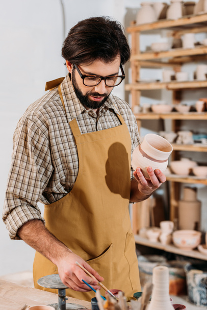 male potter painting traditional ceramic dishware in workshop - Foto, imagen
