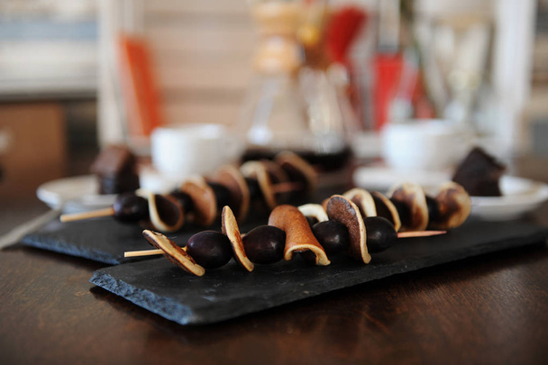 Skewers with mini pancakes and grapes on slate plates. Coffee in the filter in the background. - Photo, Image