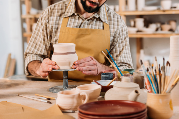 обрезанный вид человека живописи керамической посуды в керамической мастерской
 - Фото, изображение