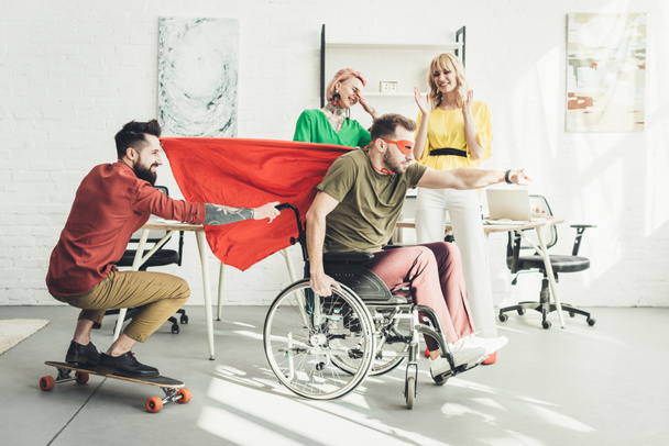 бизнесмен-инвалид в костюме супергероя с коллегой на скейтборде и бизнесвумен позади в офисе
  - Фото, изображение
