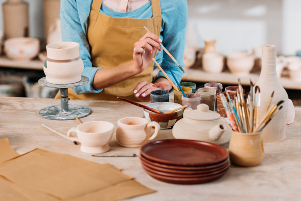 weergave van potter bijgesneden in schort schilderij keramiek serviesgoed in werkplaats - Foto, afbeelding
