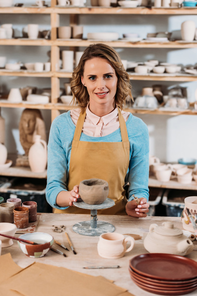 happy female potter decorating ceramic bowl in workshop  - 写真・画像