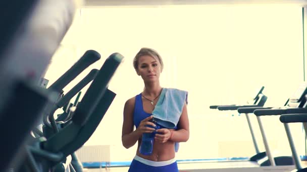 Sportwoman is drinking water from blue plastic bottle after hard training - Video, Çekim