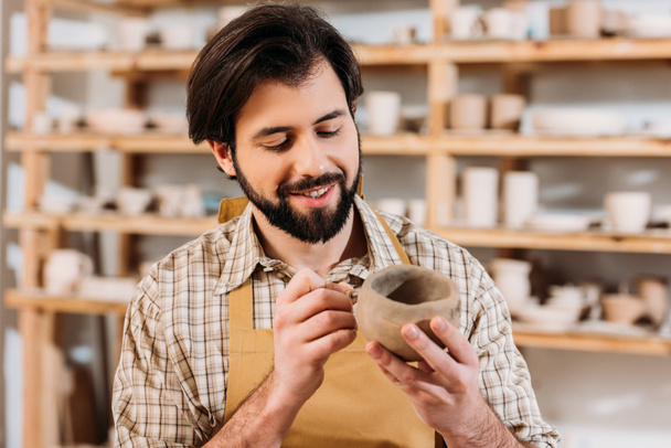 bearded man in apron decorating ceramics in pottery workshop - Photo, Image