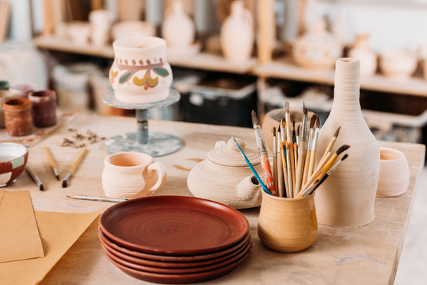 ceramic dishware and brushes on wooden table in pottery workshop - Photo, Image