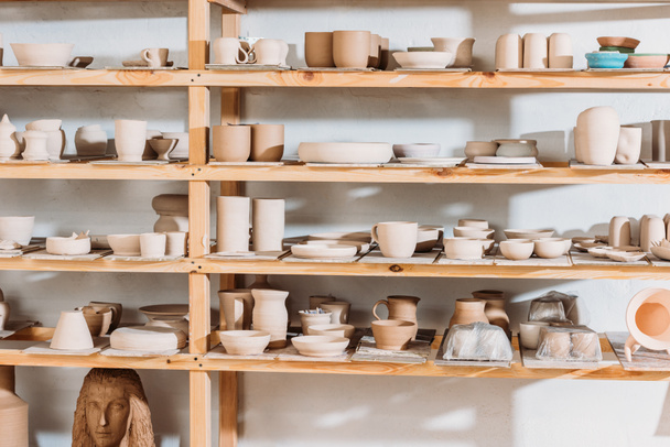 different ceramic dishware on wooden shelves in pottery workshop - Photo, Image