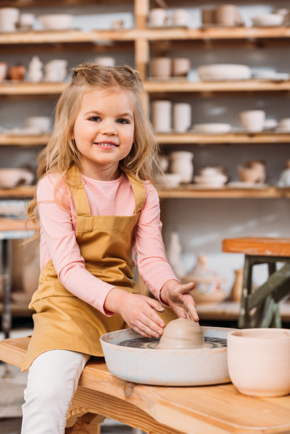 niño sonriente rubia aprendiendo a usar rueda de cerámica en el taller
 - Foto, Imagen