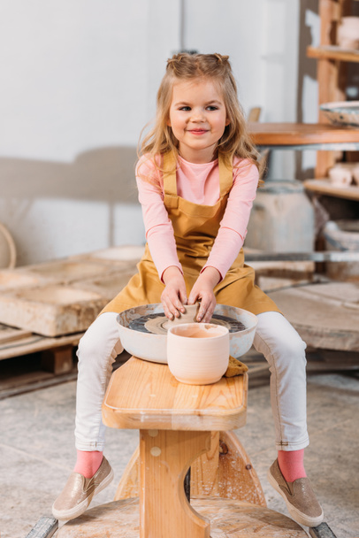blonde smiling kid making ceramics on pottery wheel in workshop - Photo, Image