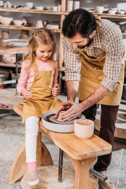 padre enseñando a su hija a usar la rueda de cerámica en el taller
 - Foto, Imagen