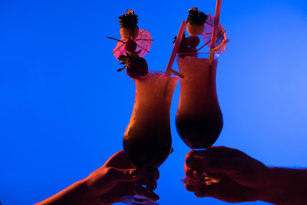 Close-up view of cocktails in male and female hands isolated on blue in dark light - Foto, Imagem