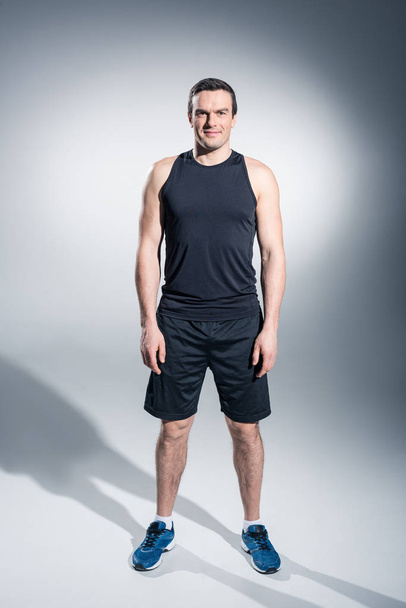 Confident sportive man in black clothes and sneakers on grey background - Valokuva, kuva