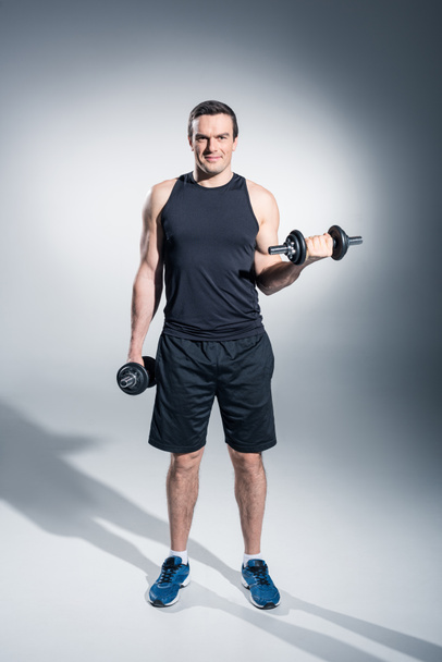Young man athlete lifting dumbbells on grey background - Foto, afbeelding