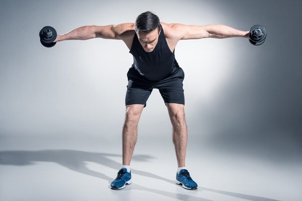 Attractive man athlete lifting dumbbells on grey background - Zdjęcie, obraz