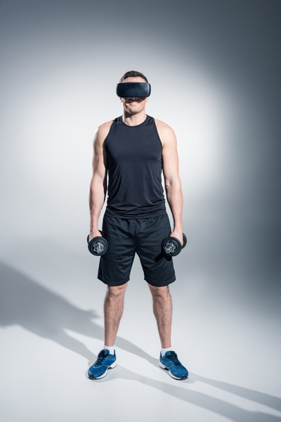 陽気な男の灰色の背景に vr メガネを着用しながらダンベル運動 - 写真・画像