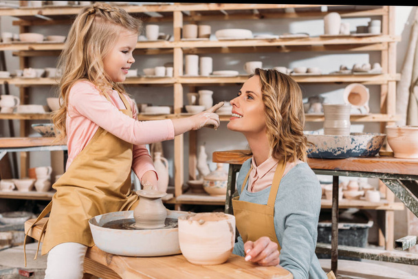 urocza córka szczęśliwy, dotykając nosa matki w pracowni ceramiki - Zdjęcie, obraz
