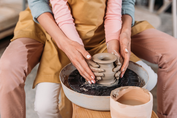 vista recortada de maestro y niño haciendo olla de cerámica juntos en la rueda de cerámica
 - Foto, imagen