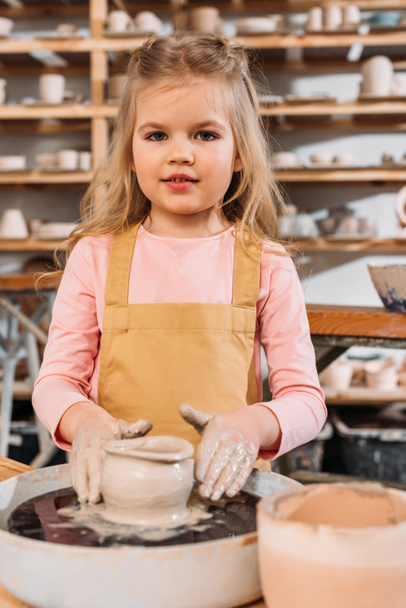 Kleines Kind bastelt Keramiktopf mit Ton auf Töpferscheibe in Werkstatt - Foto, Bild