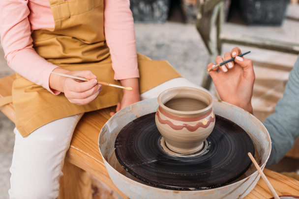 обрезанный вид учителя и ребенка живописи керамический горшок на гончарном круге в мастерской
 - Фото, изображение